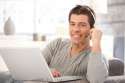 8398123-Happy-guy-using-headset-and-laptop-computer-chatting-on-Internet-smiling-at-camera--Stock-Photo.jpg