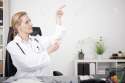 38964790-Sitting-Female-Doctor-at-her-Office-Pointing-to-Upper-Right-Side-with-Text-Space-Emphasizing-Adverti-Stock-Photo.jpg